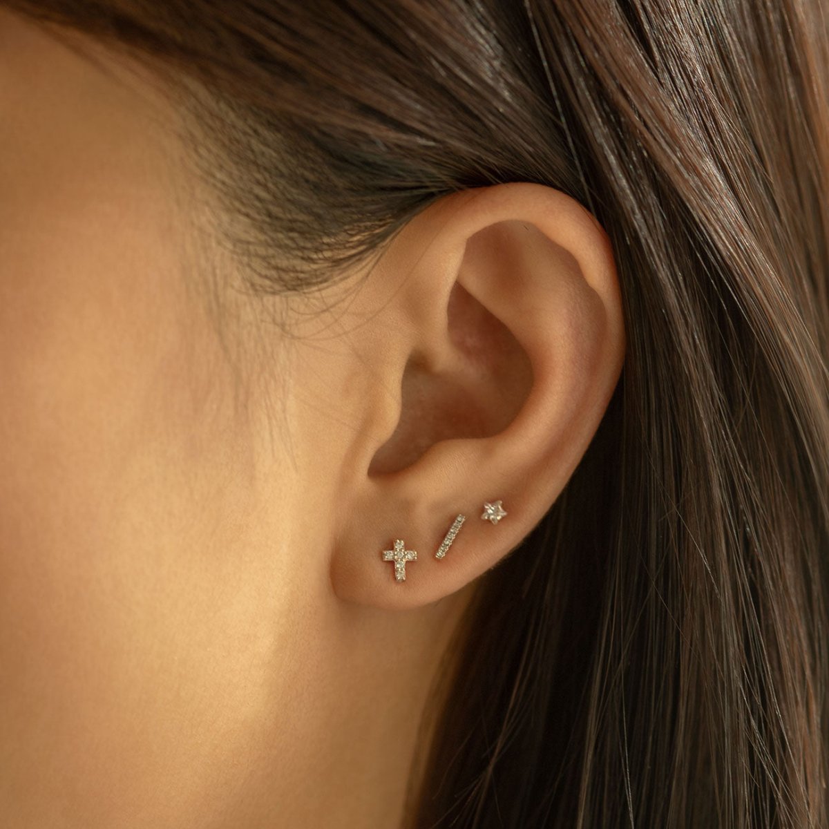 14K white gold pavé zirconia cross stud shown on a model's lobe in an ear stack