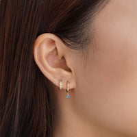 Close-up on woman's ear featuring 14K Gold Gemstone Dangle Huggies Aquamarine Cubic Zirconia paired with huggie earring