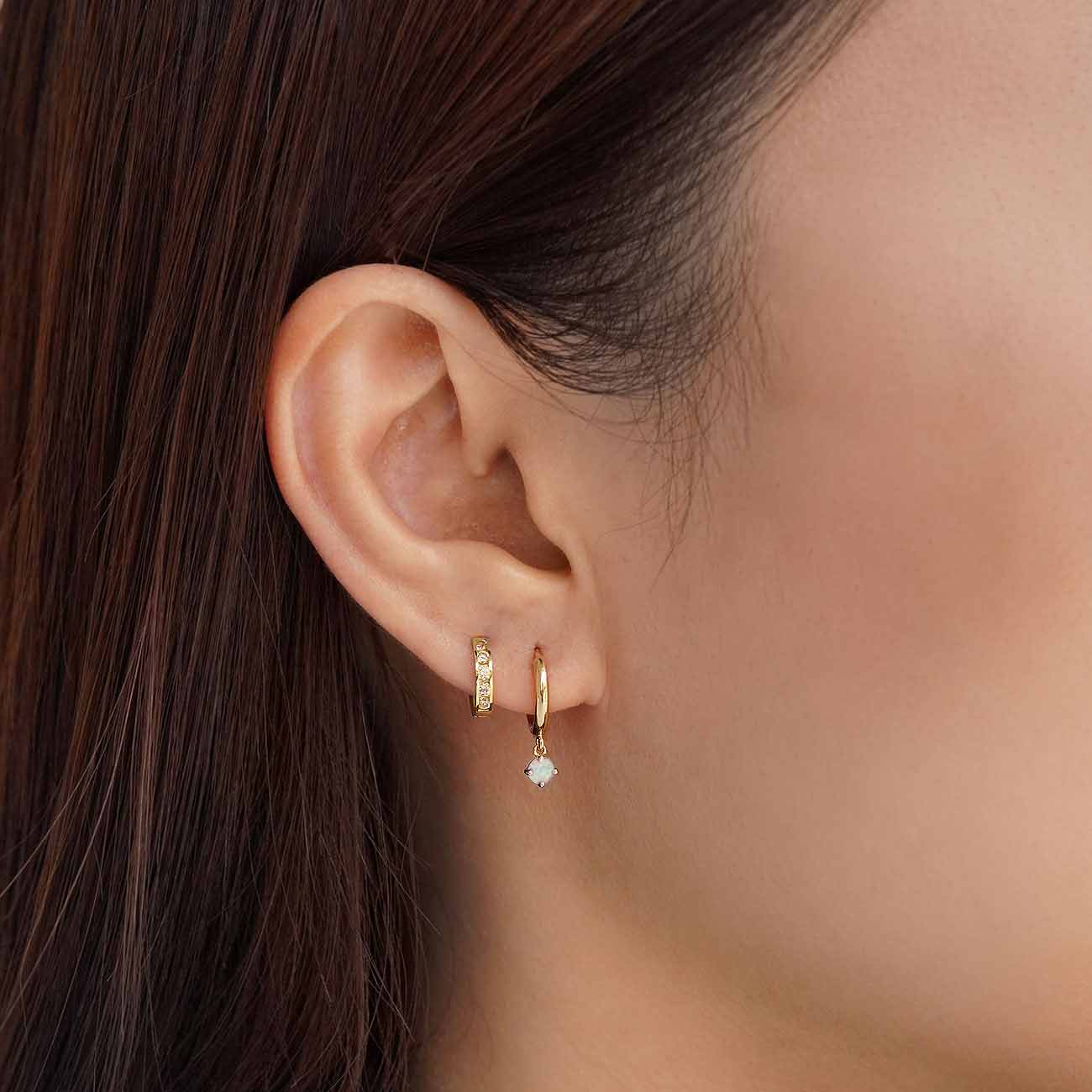 Close-up of woman's ear featuring 14K Gold Gemstone Dangle Huggies Opal paired with 14K Pave Huggie Earring 