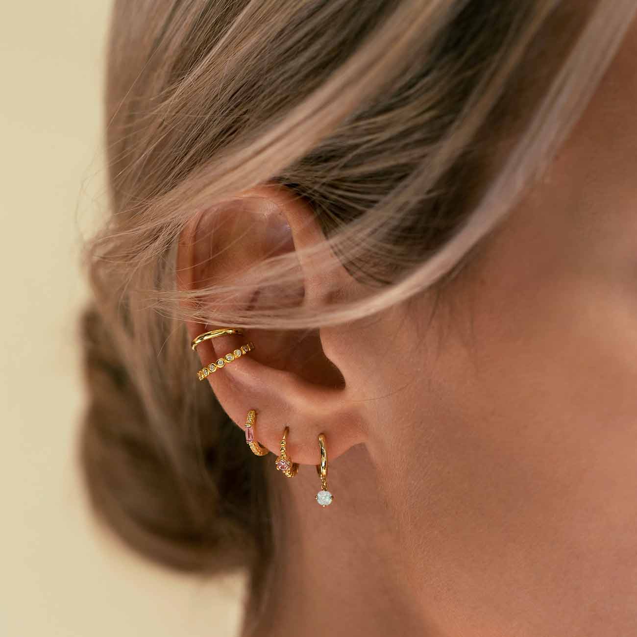 Close-up on woman's ear featuring 14K Gold Gemstone Dangle Huggies Opal and other gold huggies and ear cuffs