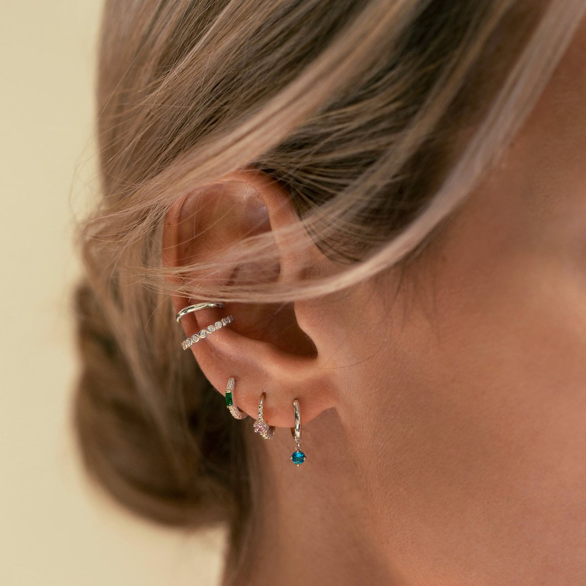 Close-up of woman's ear stack featuring Sterling Silver Gemstone Bead Huggies Pink CZ Crystal and other gemstone earrings. 