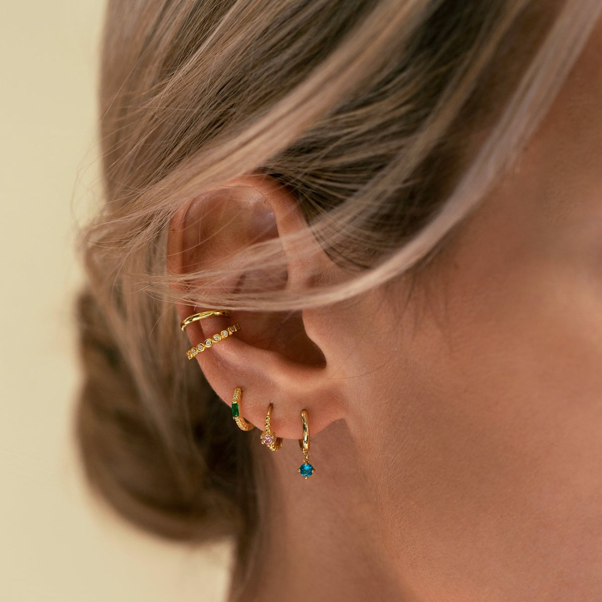 Close-up on woman's ear featuring Gold Vermeil Gemstone Baguette Huggie Earrings Emerald and other gemstone earrings. 