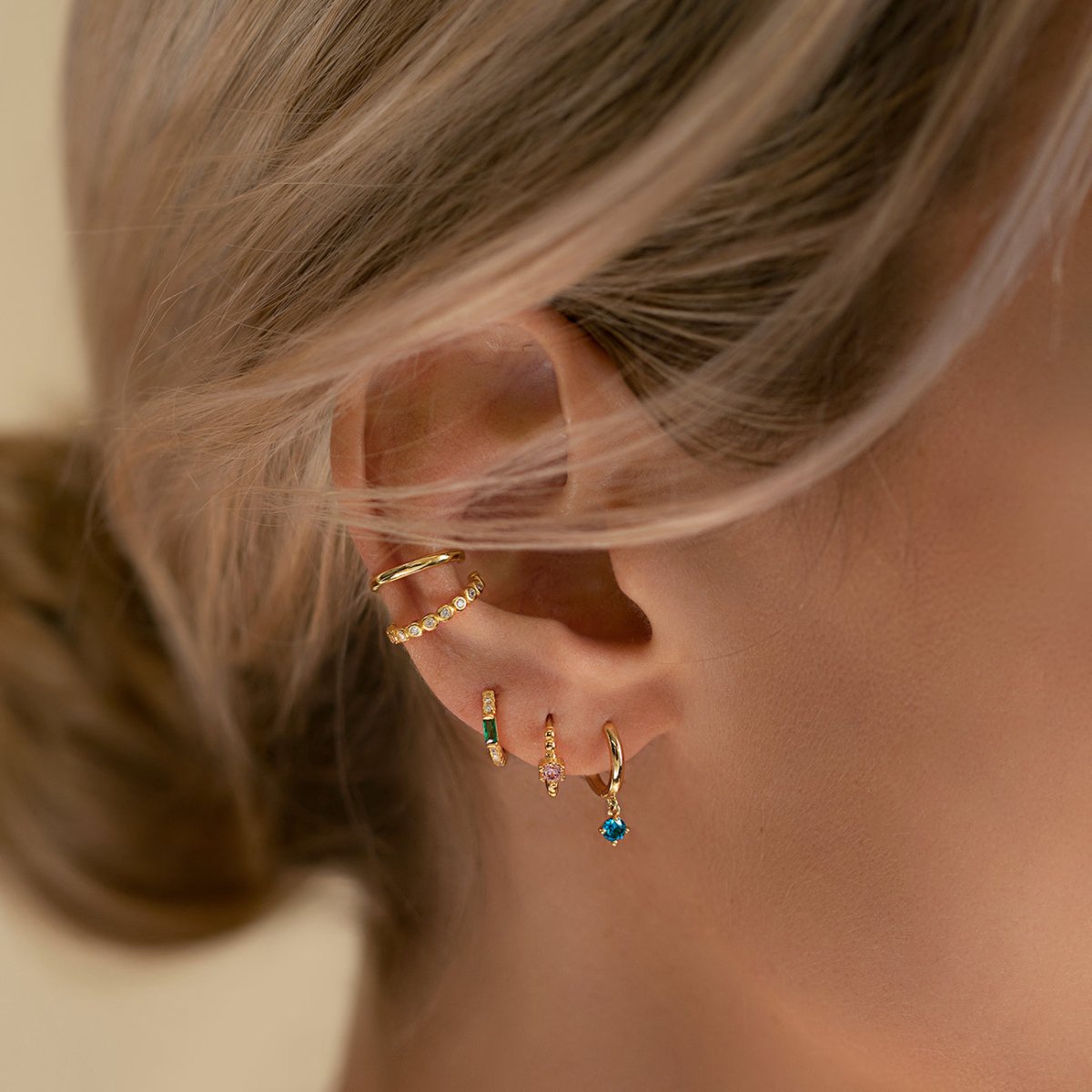 Close-up on woman's ear featuring Gold Vermeil Gemstone Baguette Huggie Earrings Emerald and other gemstone earrings. 