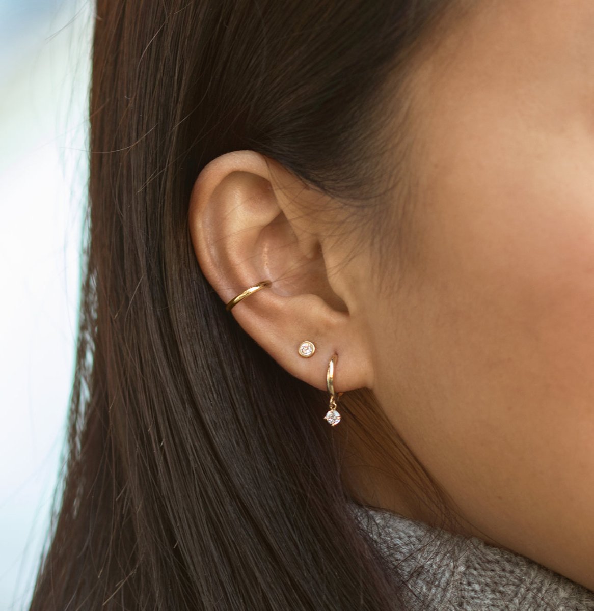 Close-up of woman's ear featuring 14K Gold Gemstone Dangle Huggies Moissanite paired with stud earring 