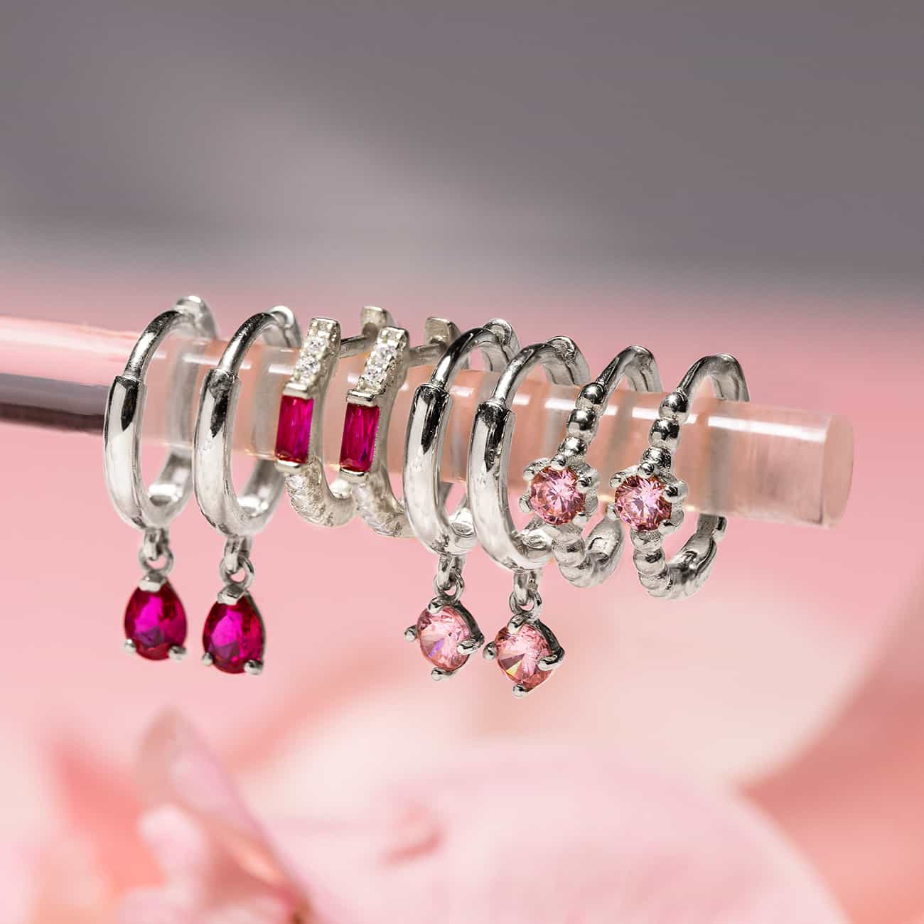 Close-up on earrings featuring Sterling Silver Gemstone Baguette Huggie Ruby + Pink Earrings. 