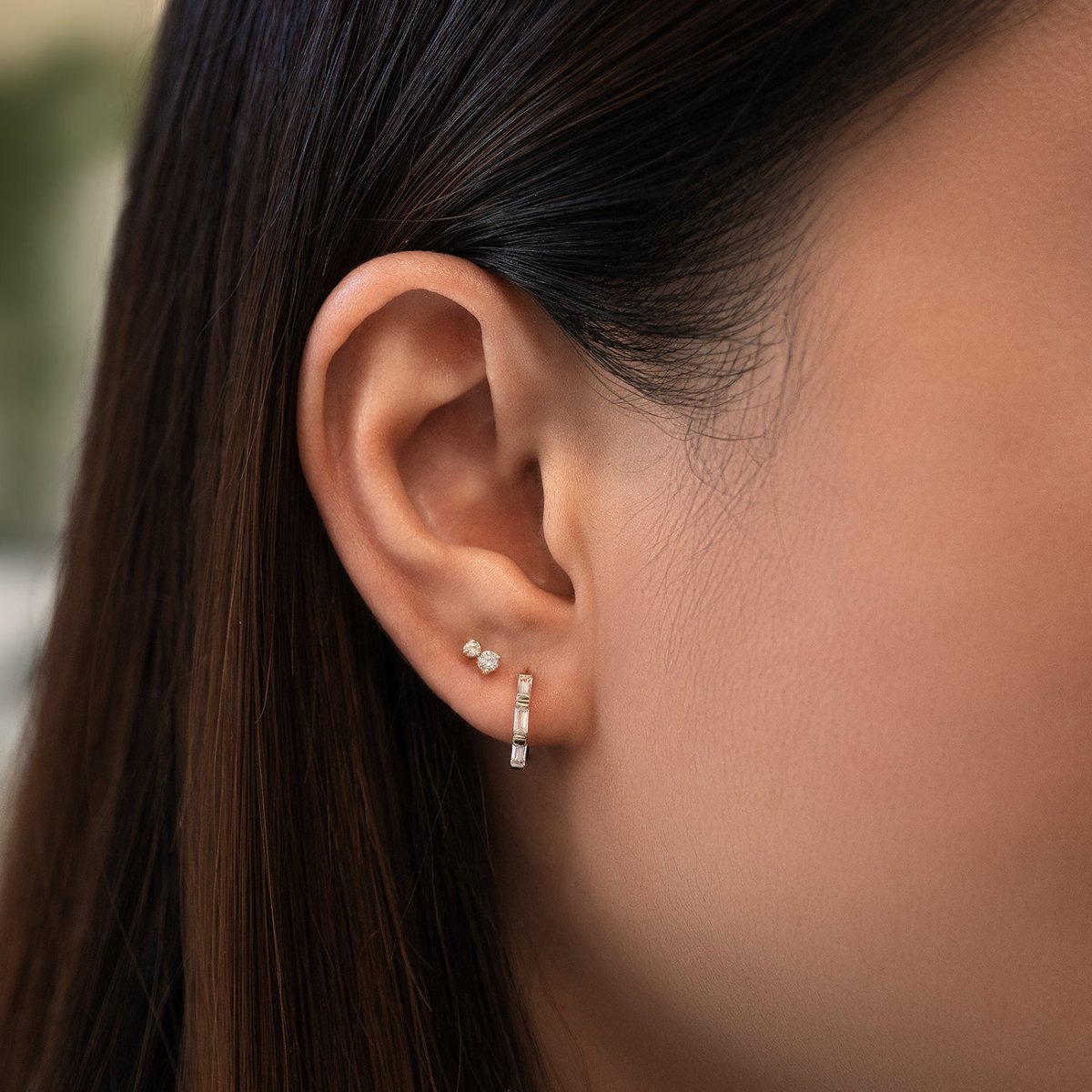 Close-up of woman's ear featuring 14K Solid White Gold Tri Baguette Huggie Hoops Moissanite Crystal paired with stud earring