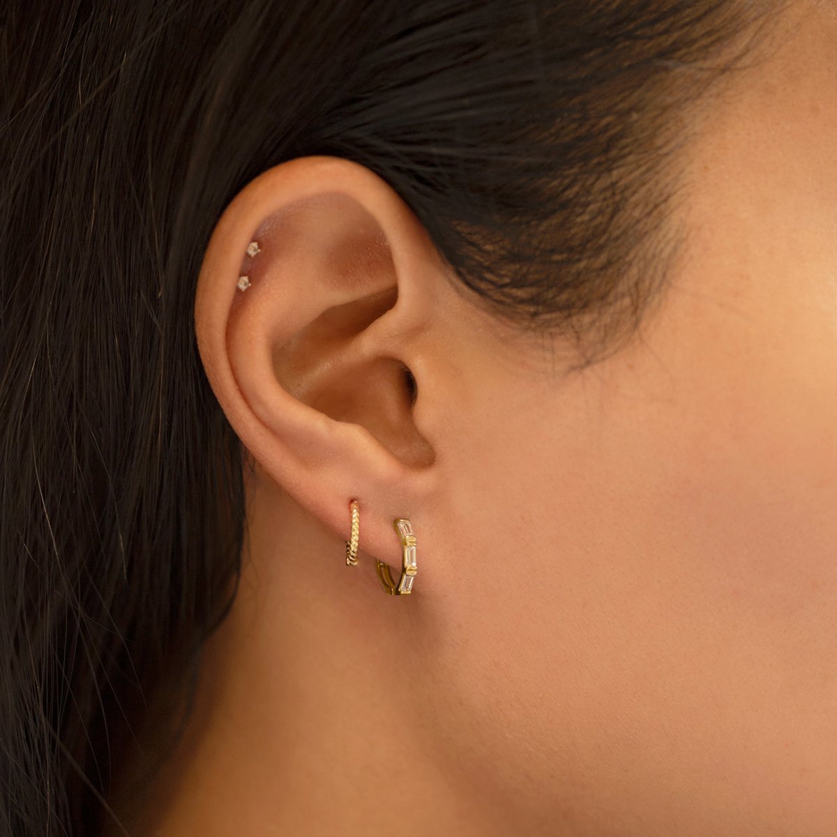 Close-up of woman's ear featuring 14K Solid Gold Tri Baguette Huggie Hoops Moissanite Crystals and 14K Small Rope Huggie Earring