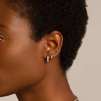 Close-up of woman's ear featuring 14K White Gold Octagon Huggie Earrings, Pave Huggie Earring, Sphere Huggie Earring, and Tiny Crystal Stud Set 