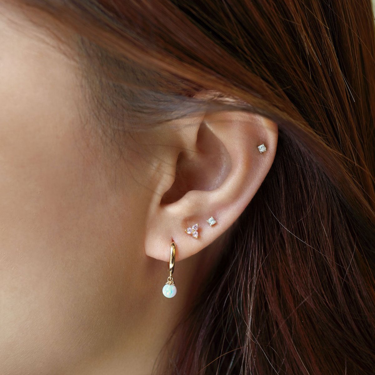 Close-up of woman's ear featuring 14K Gold Tiny Opal Huggies and stud earrings