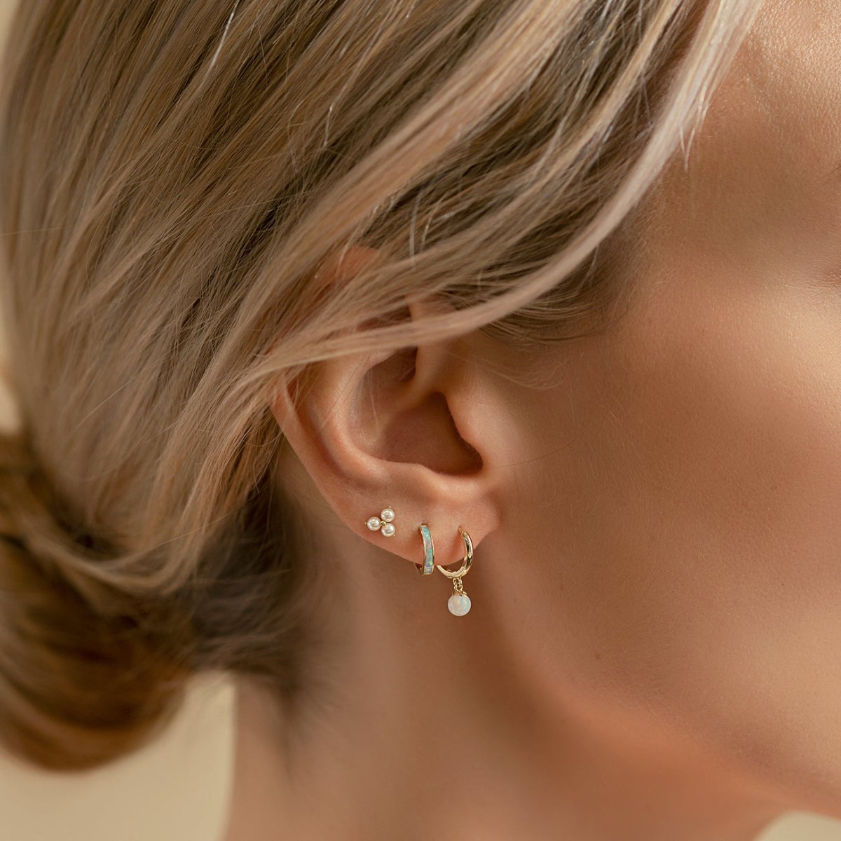 Close-up of woman's ear featuring 14K Gold Tiny Opal Huggies and stud earrings