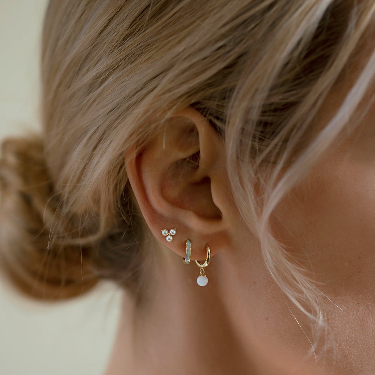 Close-up of woman's ear featuring 14K Gold Tiny Opal Huggies and stud earrings