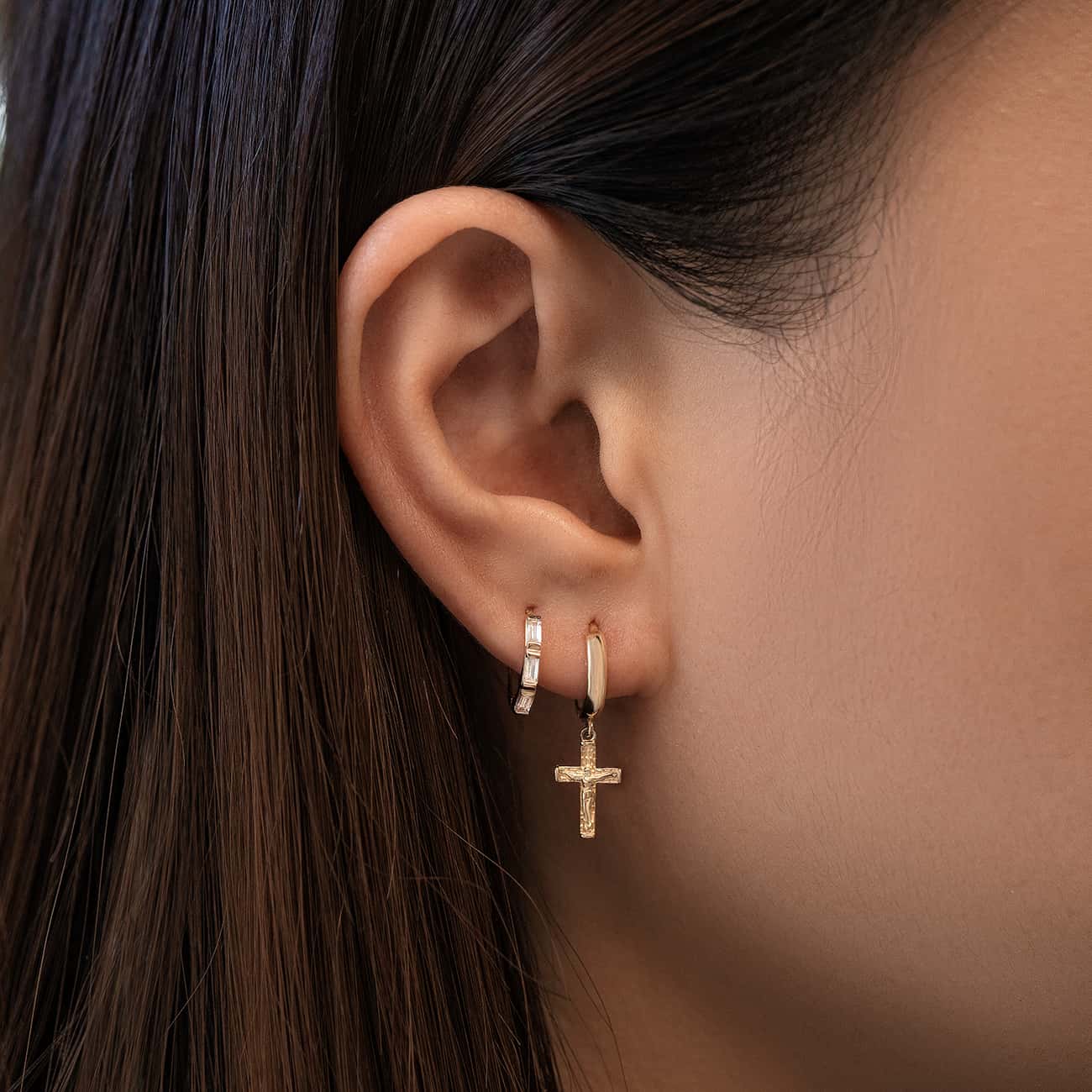 Close-up of woman's ear featuring 14K Solid Gold Tri Baguette Huggie Hoops Moissanite Crystals and 14K Cross Drop Huggie Earring