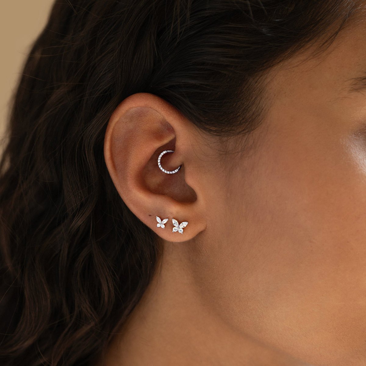 Close-up of an ear with butterfly-shaped earrings and a hoop earring, daith piercing earring