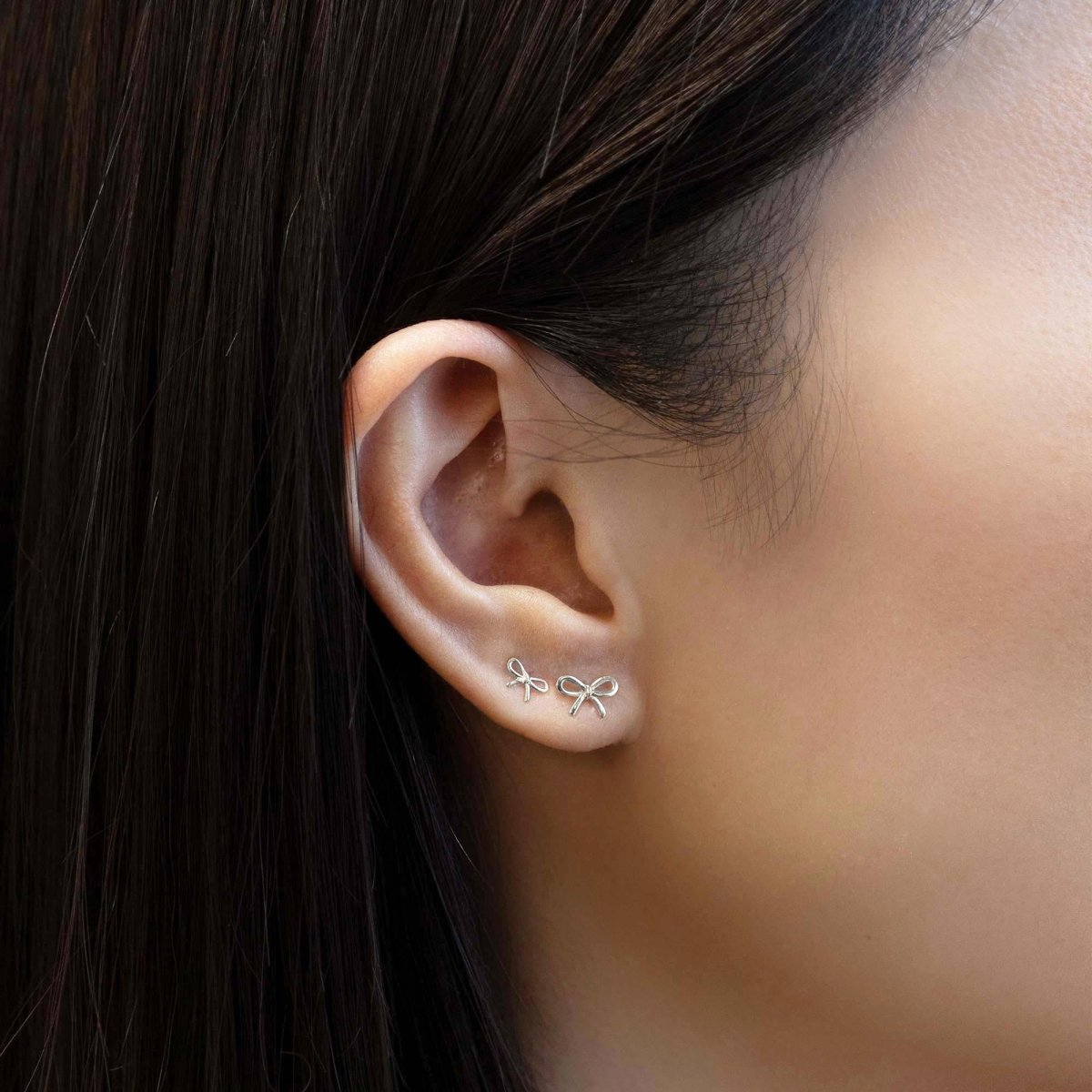 Close up of woman's ear featuring different sized 14K White Gold Tiny Bow Single Stud