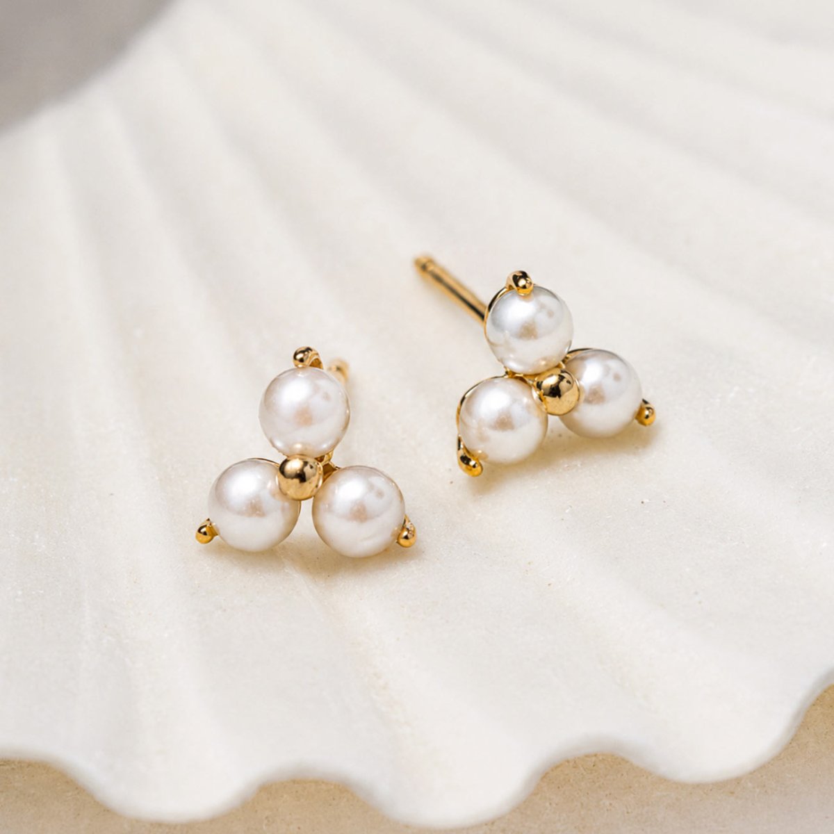 Pearl Trinity Studs 14K Gold featuring three freshwater pearls in a triangular design displayed on a white seashell.
