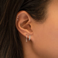 Close-up of woman wearing 14k white gold birthstone U huggies, silver star flare huggie earrings, and 14k white gold tiny sphere studs