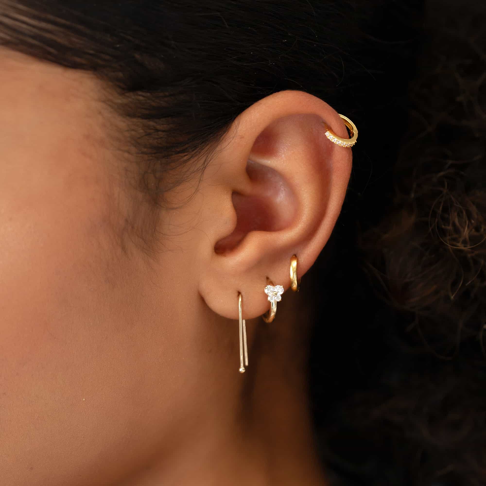 Close-up of woman's ear featuring 14K Gold Single Thin Pave Huggie and other dainty gold earrings. 