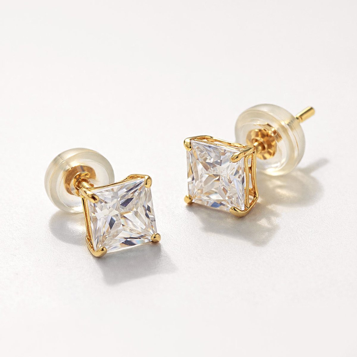 Detailed shot of AMYO's 14K Gold Princess Cut stud earrings with white zirconia gemstone and silicone earring backs.