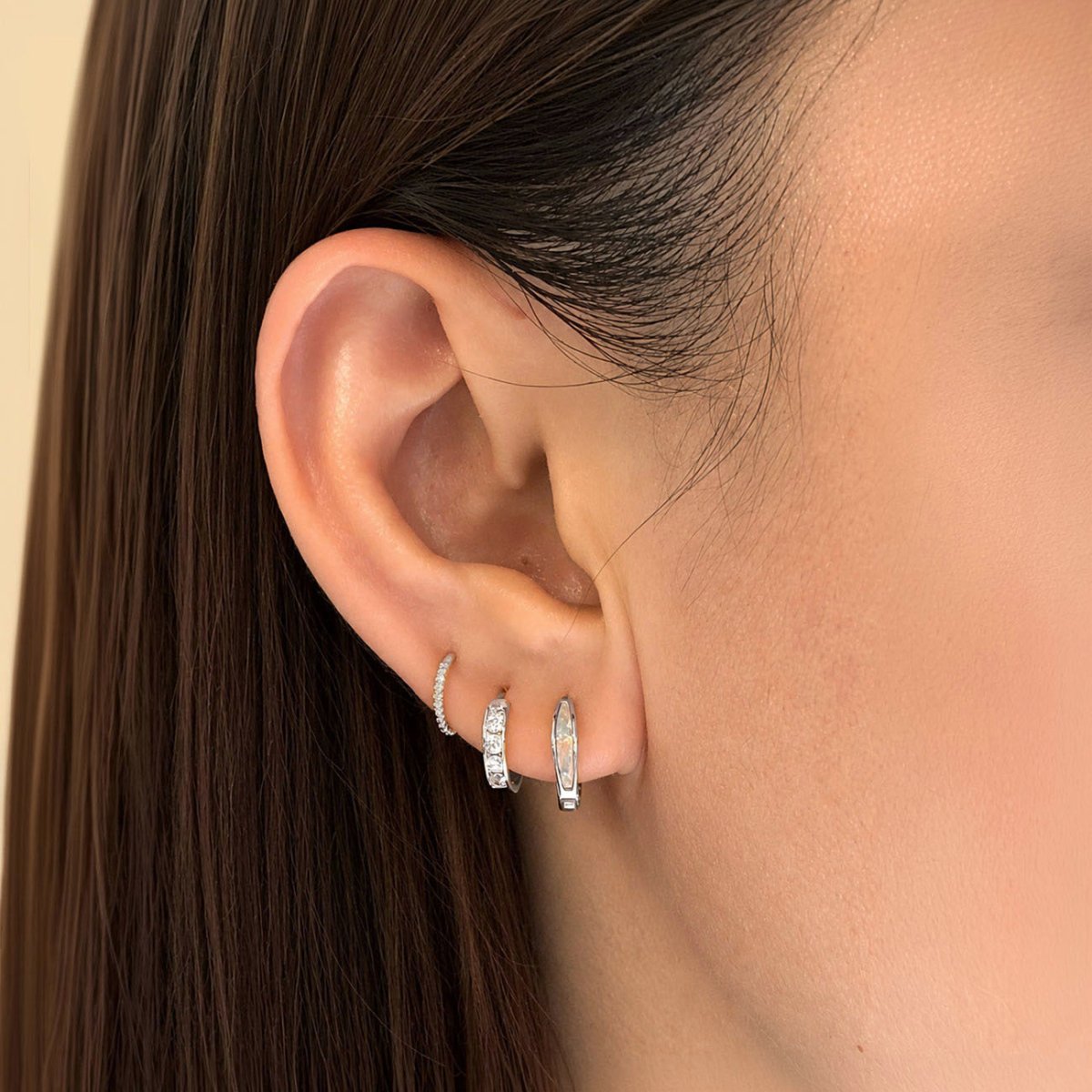 Three 14K white gold huggie hoops worn in a stacked lobe piercings, including a stone-set huggie