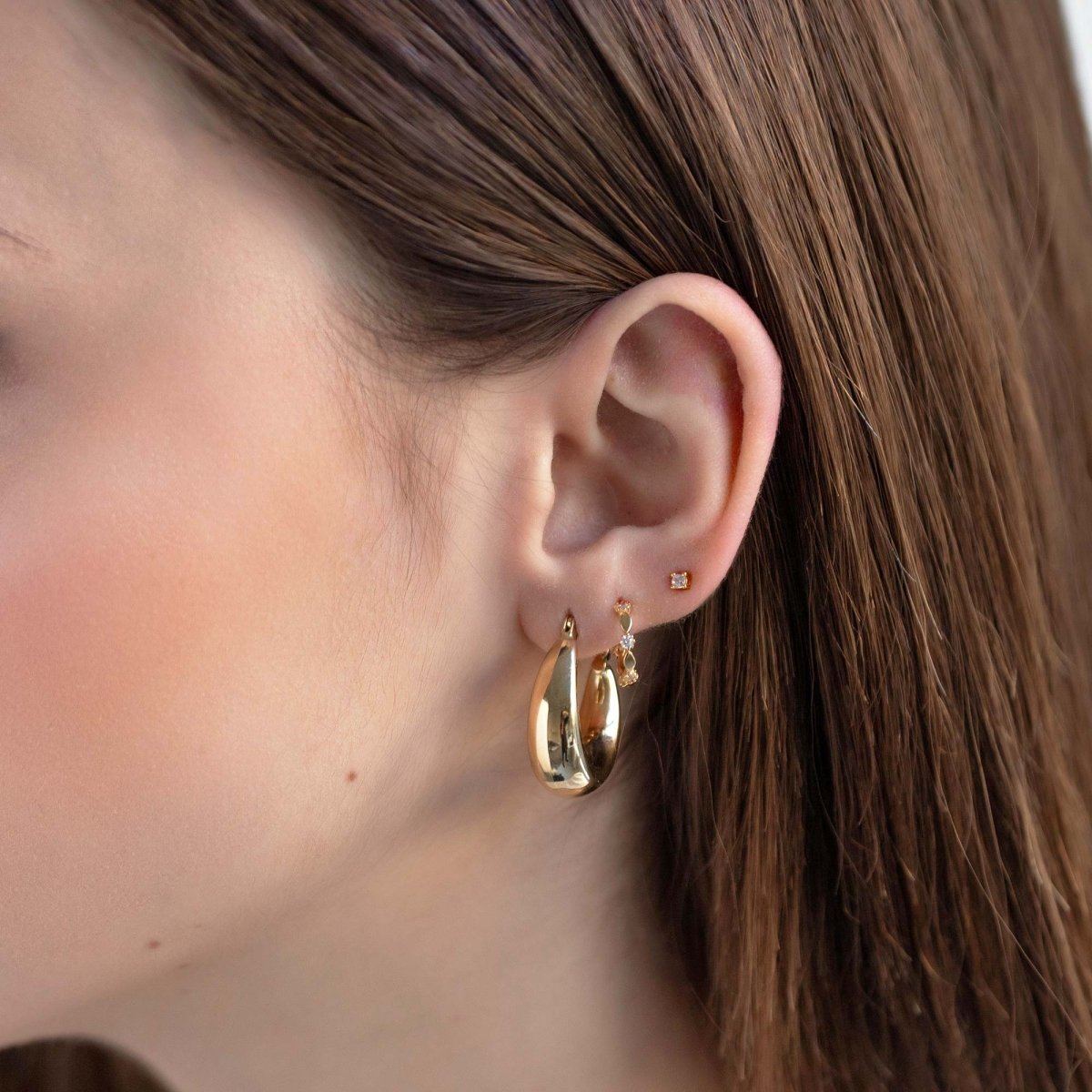 14K gold U-shaped bubble hoops shown on a model's lobe with tiny stud earrings