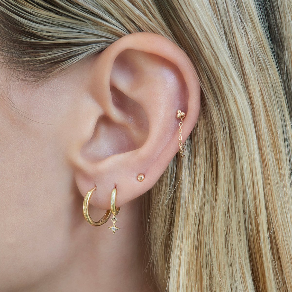 Close-up of woman's ear featuring 14K Gold Tiny Sphere Studs paired with hoop earrings 