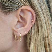 Close-up of woman's ear featuring Tiny 14K Solid Gold Sphere Studs paired with hoop earrings 