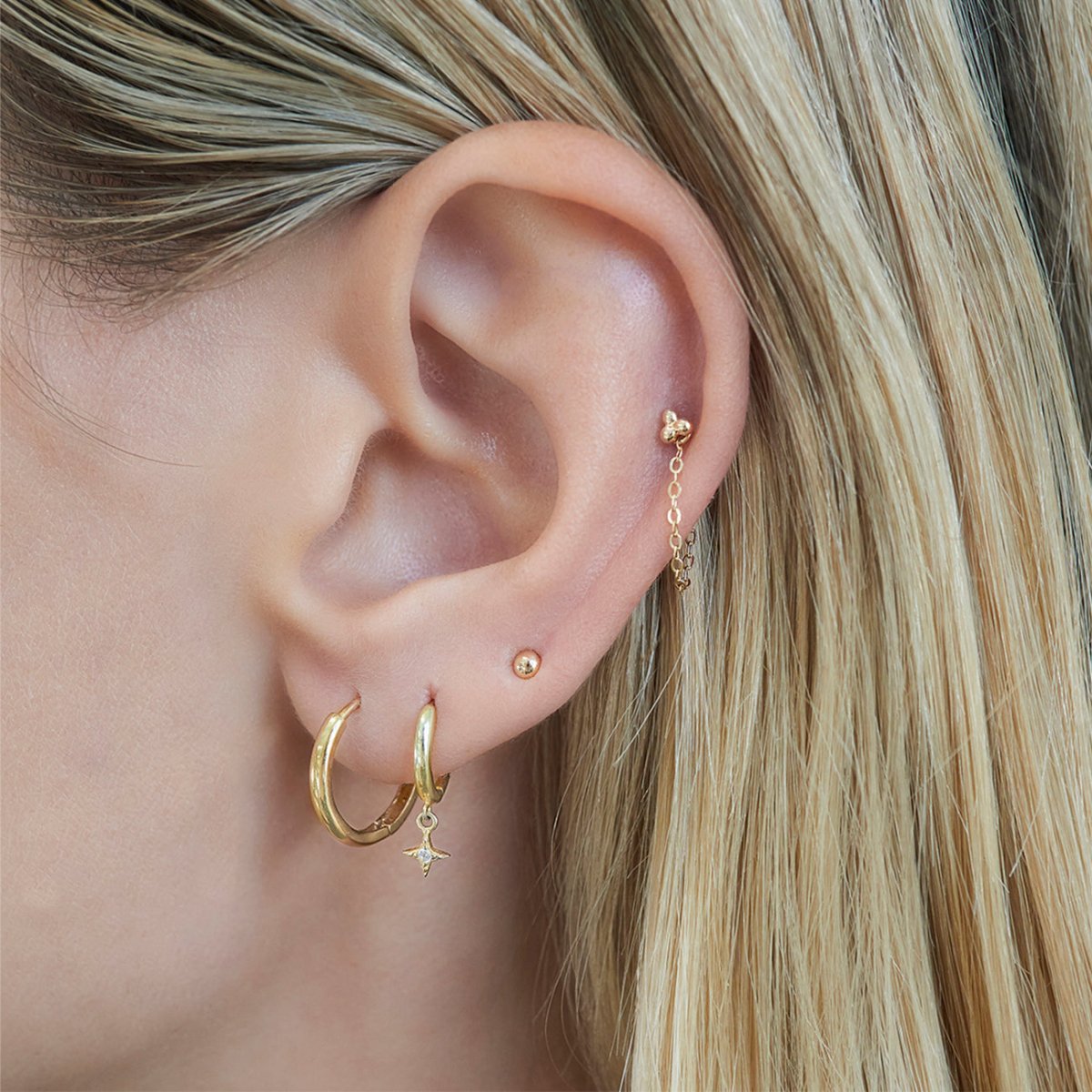 Close-up of woman's ear featuring Tiny 14K Solid Gold Sphere Studs paired with hoop earrings 