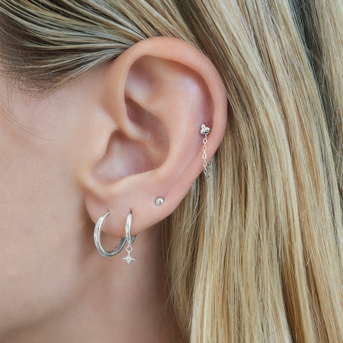 Close-up of woman's ear featuring Tiny 14K White Gold Sphere Studs paired with hoop earrings 