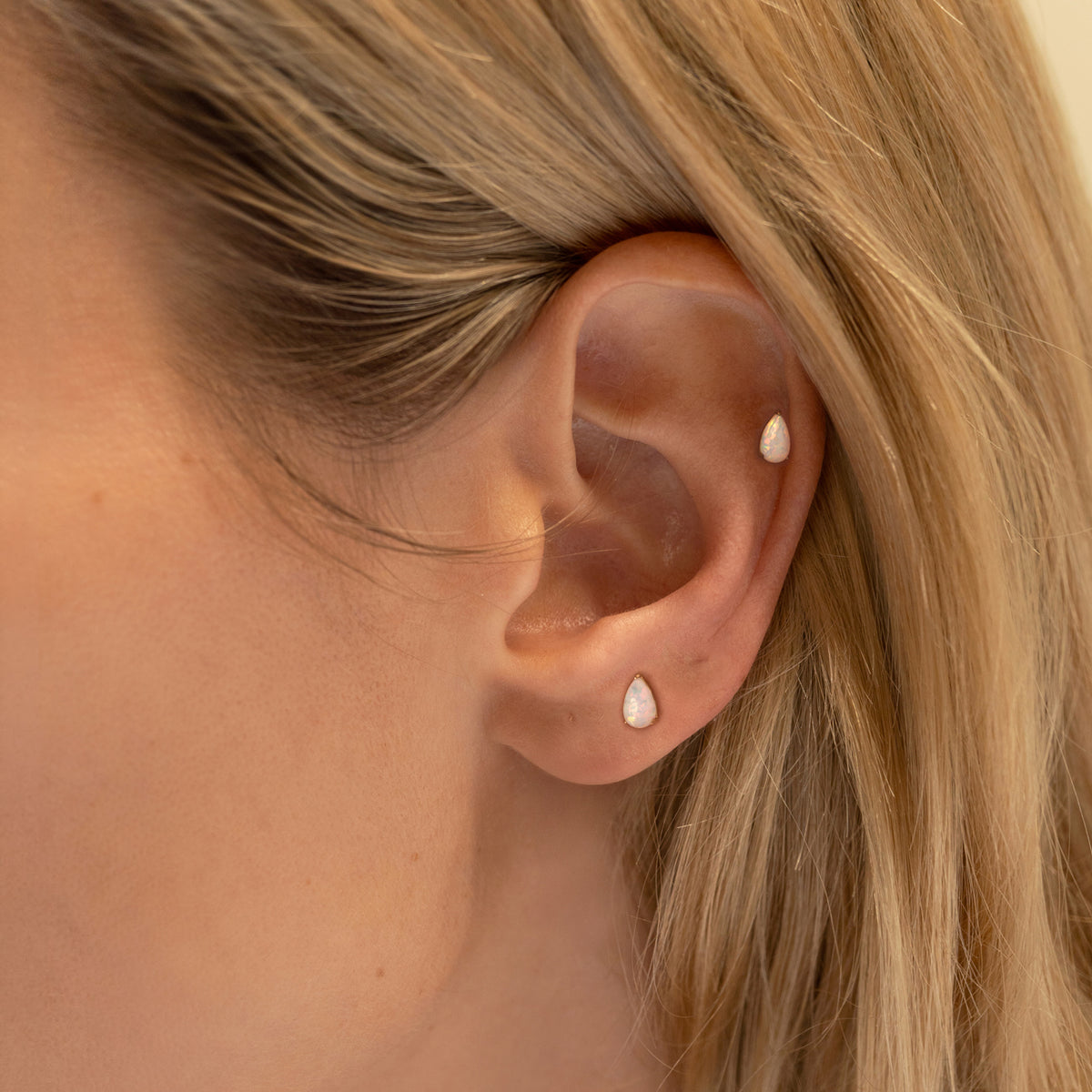 Ear worn with two pear-shaped white stone flat back studs in the lobe and helix piercings