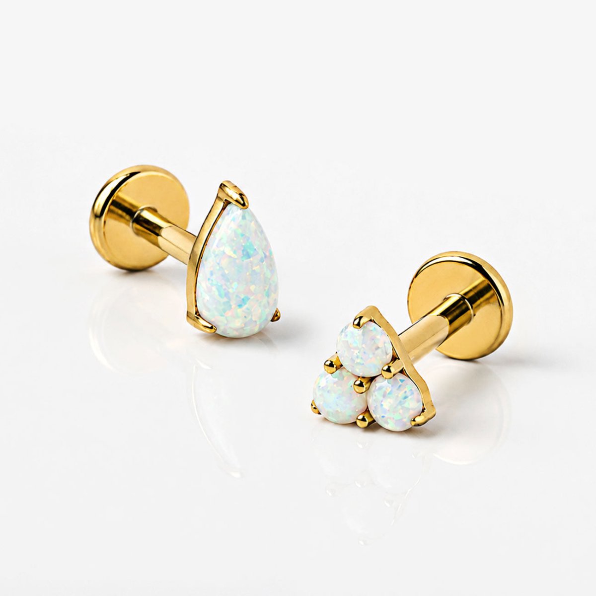 Gold opal flat back earrings with pear and trinity designs on grey background.