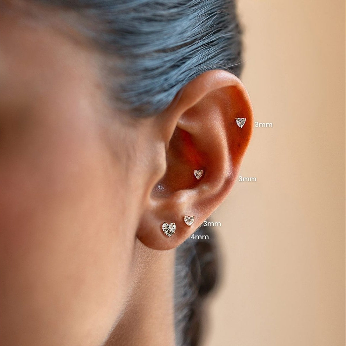 Four gold heart crystal flat back studs worn along a model's ear, labeled 3mm and 4mm