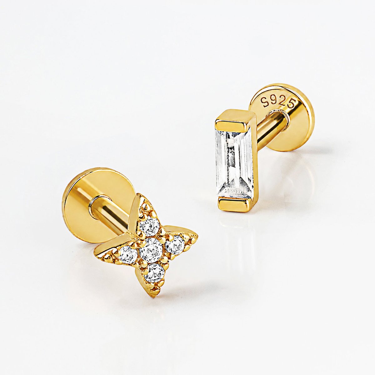 Two gold flat back studs on a white surface, one crystal star and one baguette crystal bar