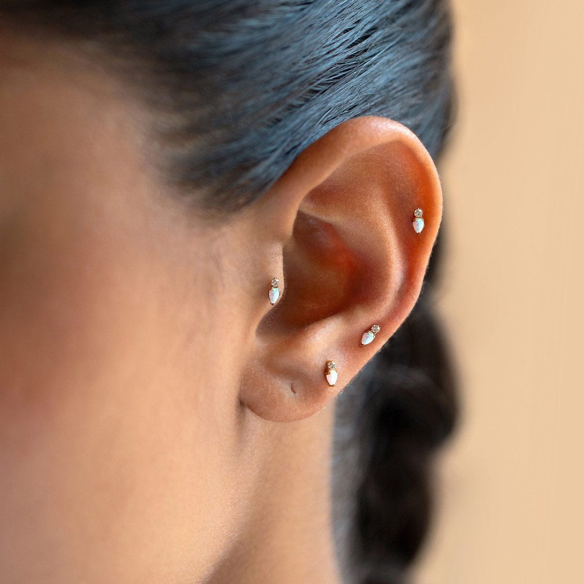 Gold flat back stud earrings with a round crystal and pear-shaped opal gemstone, shown on a model's ear. | #Gemstone_White Opal