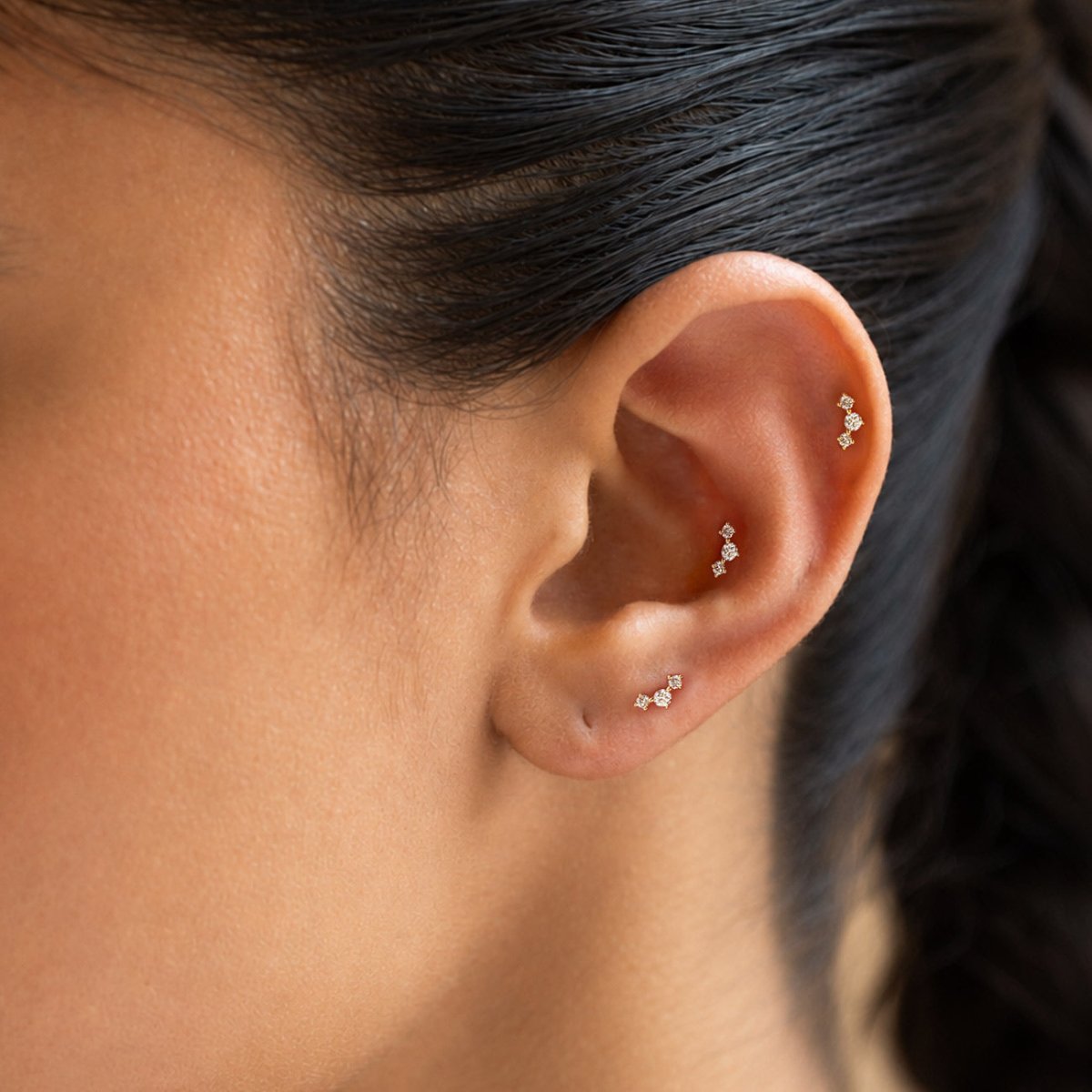 Three matching 14K gold curved three-stone flat back studs worn in lobe, conch and helix piercings