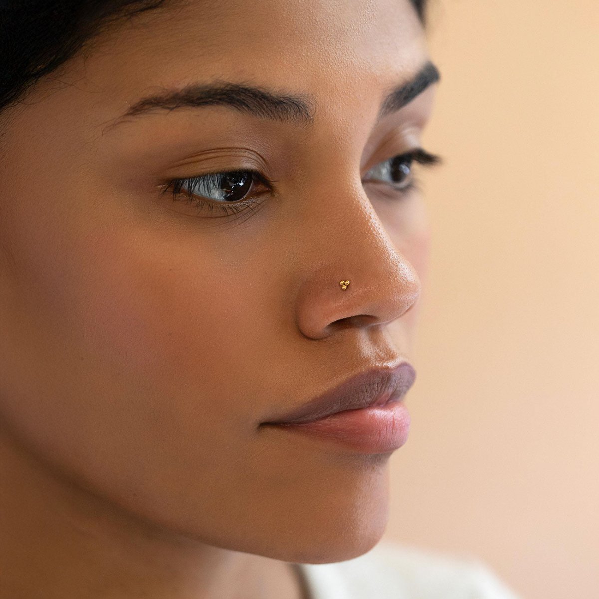 Close-up of a woman's face with a soft focus on AMYO's Tiny Trinity Ball Nose Stud
