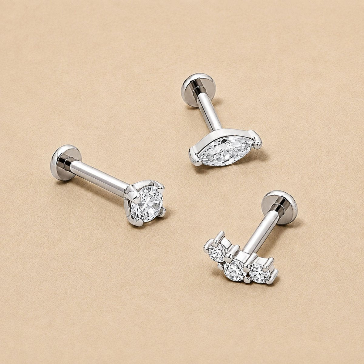 Three 14K White Gold flat back studs on a beige surface: a round crystal, a marquise crystal and a curved three-stone crown