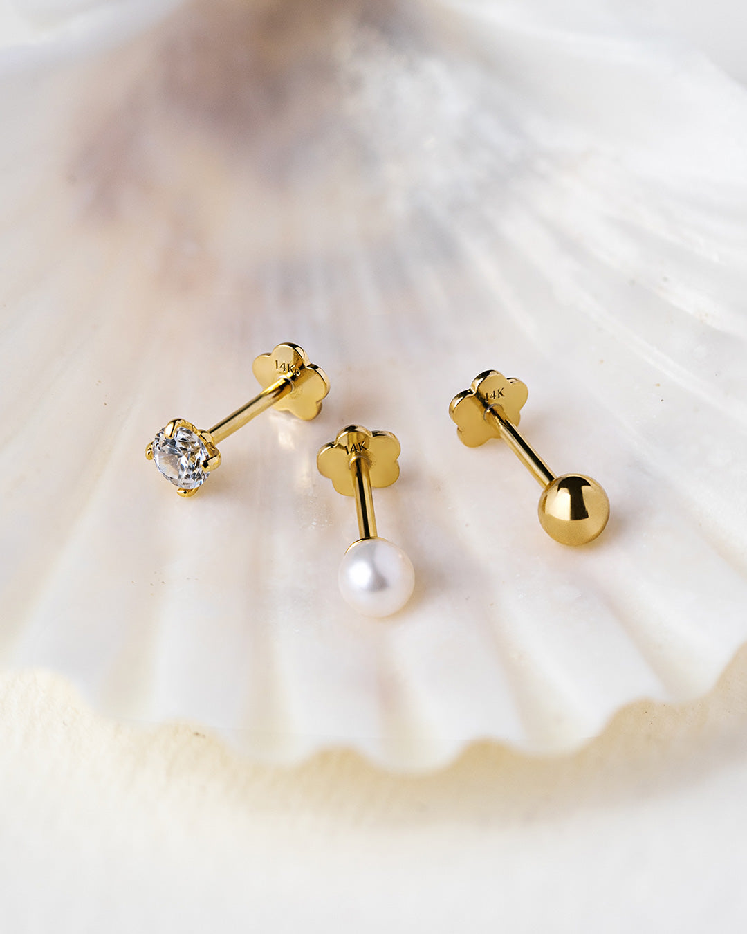 Shop AMYO 14k gold flat back stud earrings featuring crystal, pearl, and gold ball designs displayed on shell background.