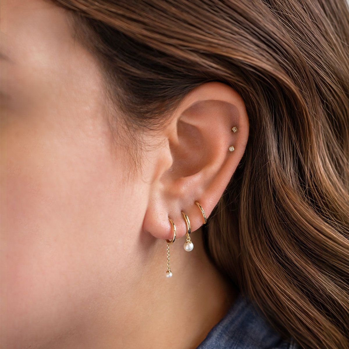 Gold ear stack with white drop huggie hoops, tiny crystal studs and cartilage earrings.
