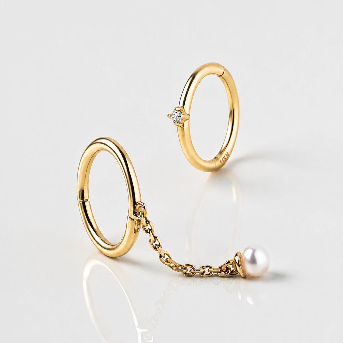Two 14K gold clicker hoops on a white surface, one set with a tiny stone, one with a chain-hung round drop