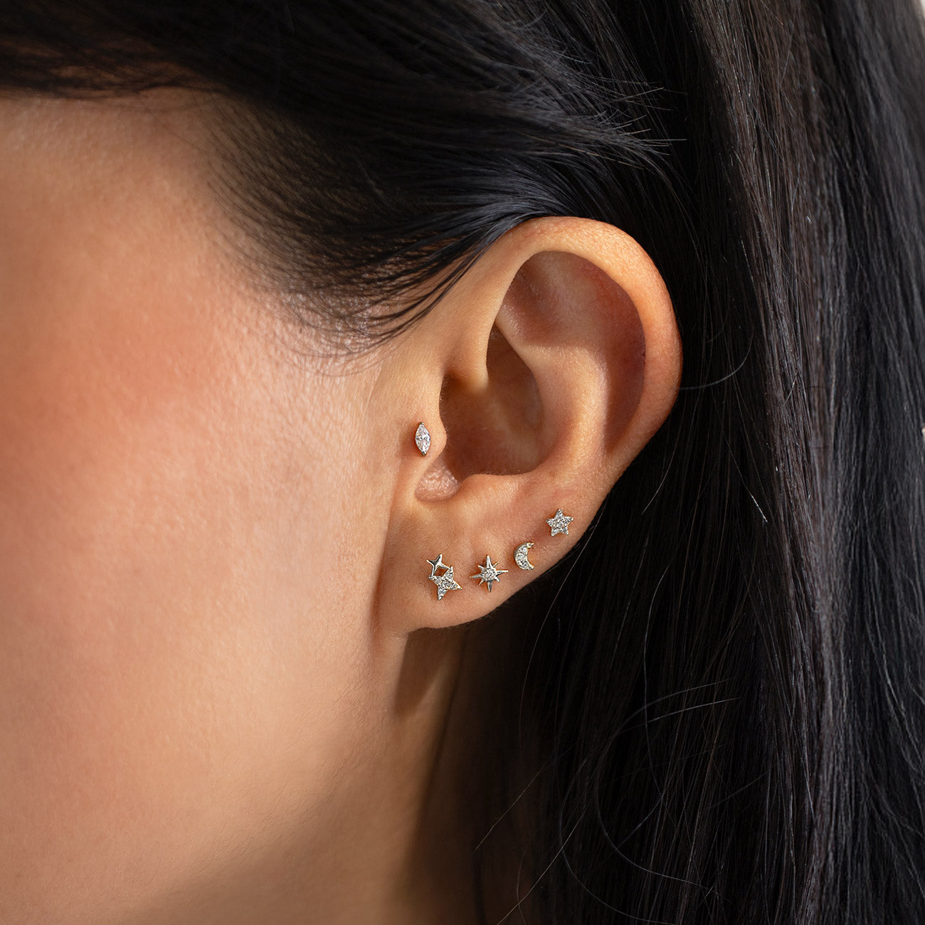 Close-up of an ear wearing multiple silver flat back stud earrings from AMYO, including the Tiny Marquise Gemstone Stud.
