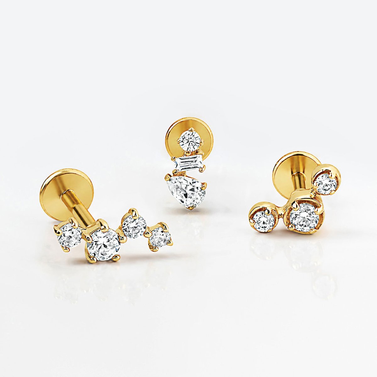 Three 14K gold flat back studs with curved, stacked and clustered crystal designs on a white surface