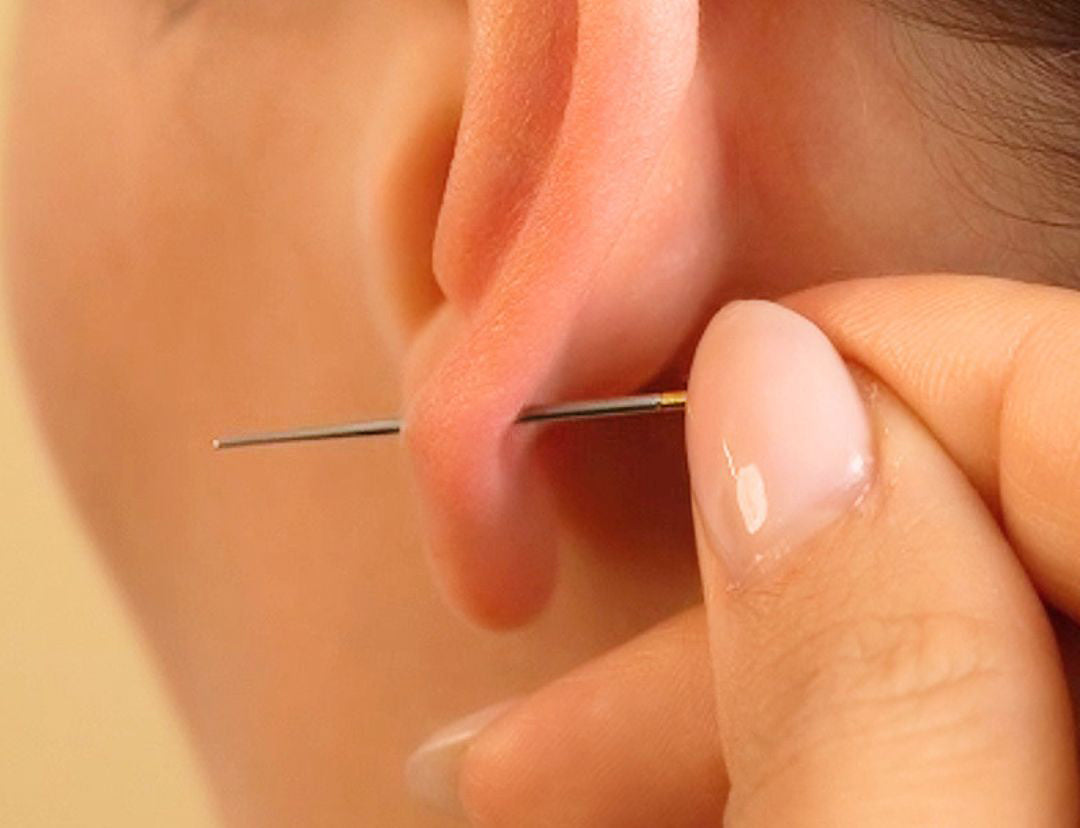 Close-up of a hand holding the flatback tool guide passing through an earlobe