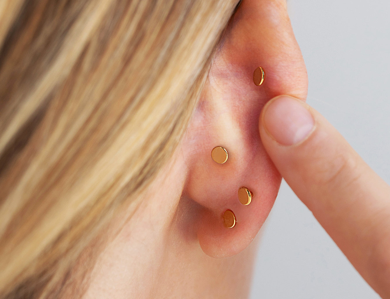 Close-up showing the flat disc backing of flat back earrings worn in multiple ear piercings.