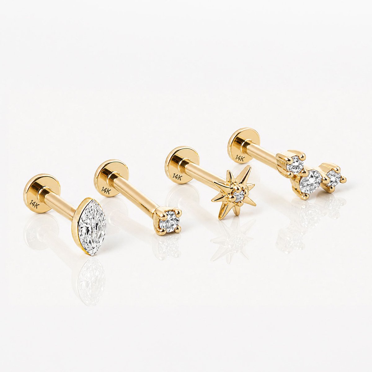 Four 14K gold flat back earrings lying on a white surface: marquise, round stone, starburst and curved trio