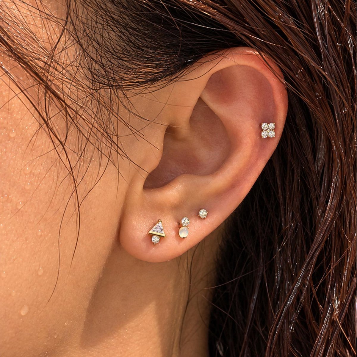 Close-up of an ear with wet hair wearing waterproof gold titanium flat back earrings in multiple lobe and cartilage piercings.|#Gemstone_White Opal