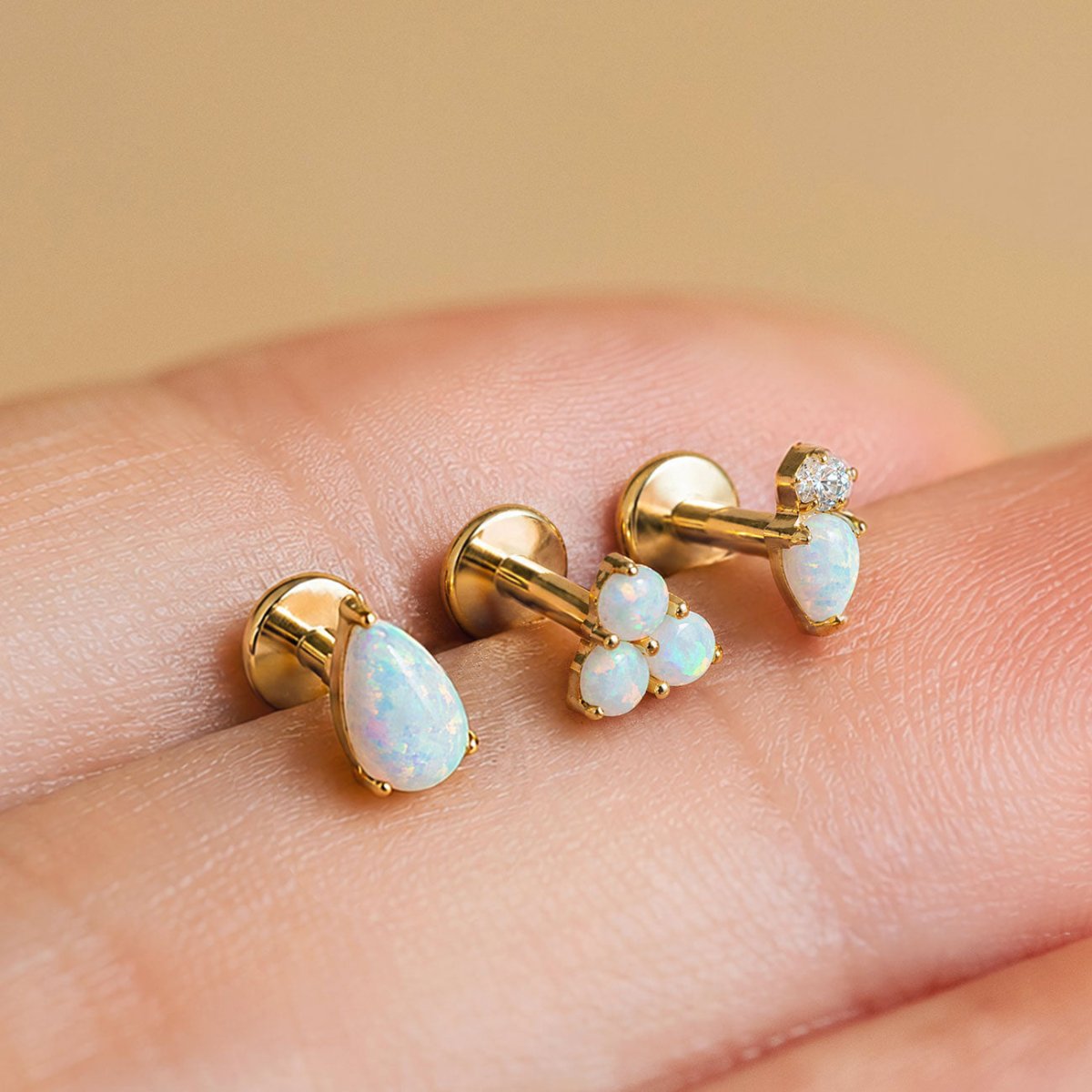 Gold opal flat back earrings with pear, trinity and crystal opal designs shown in hand.