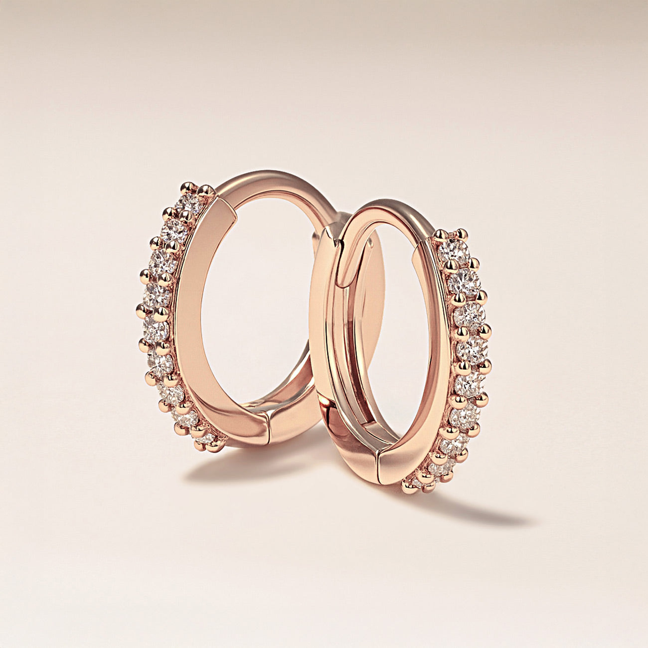 AMYO Rose gold hoop earrings with diamond accents on a light beige background