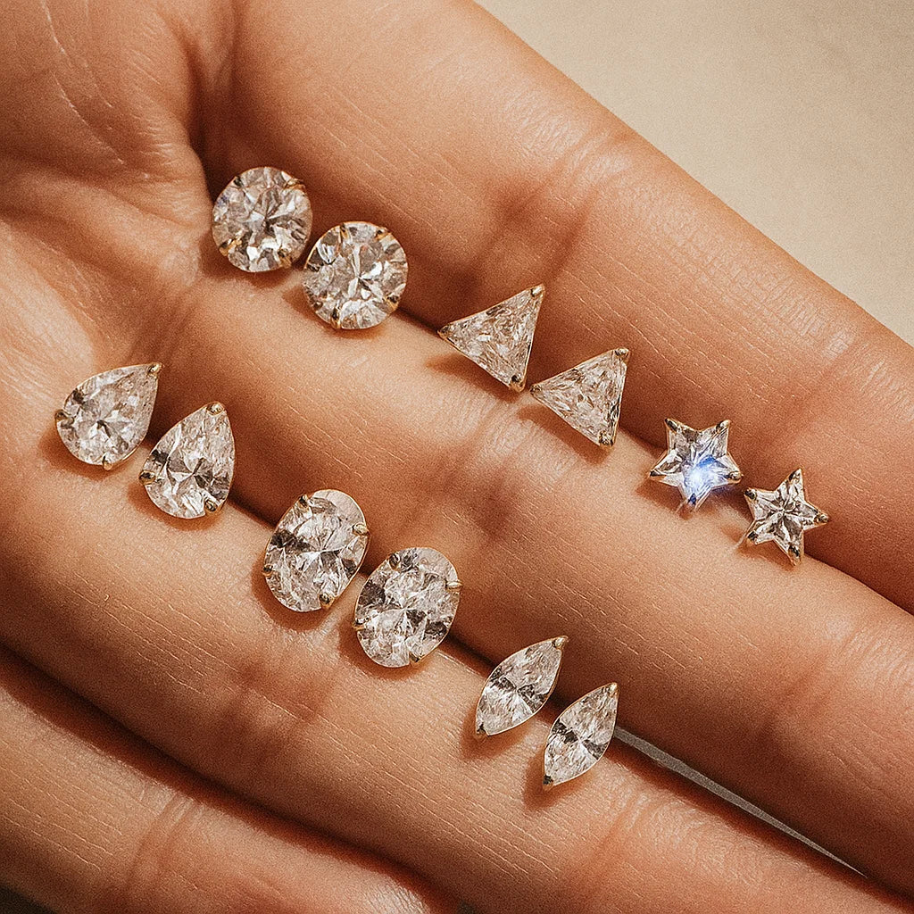 Assorted AMYO diamond earrings on a hand against a neutral background