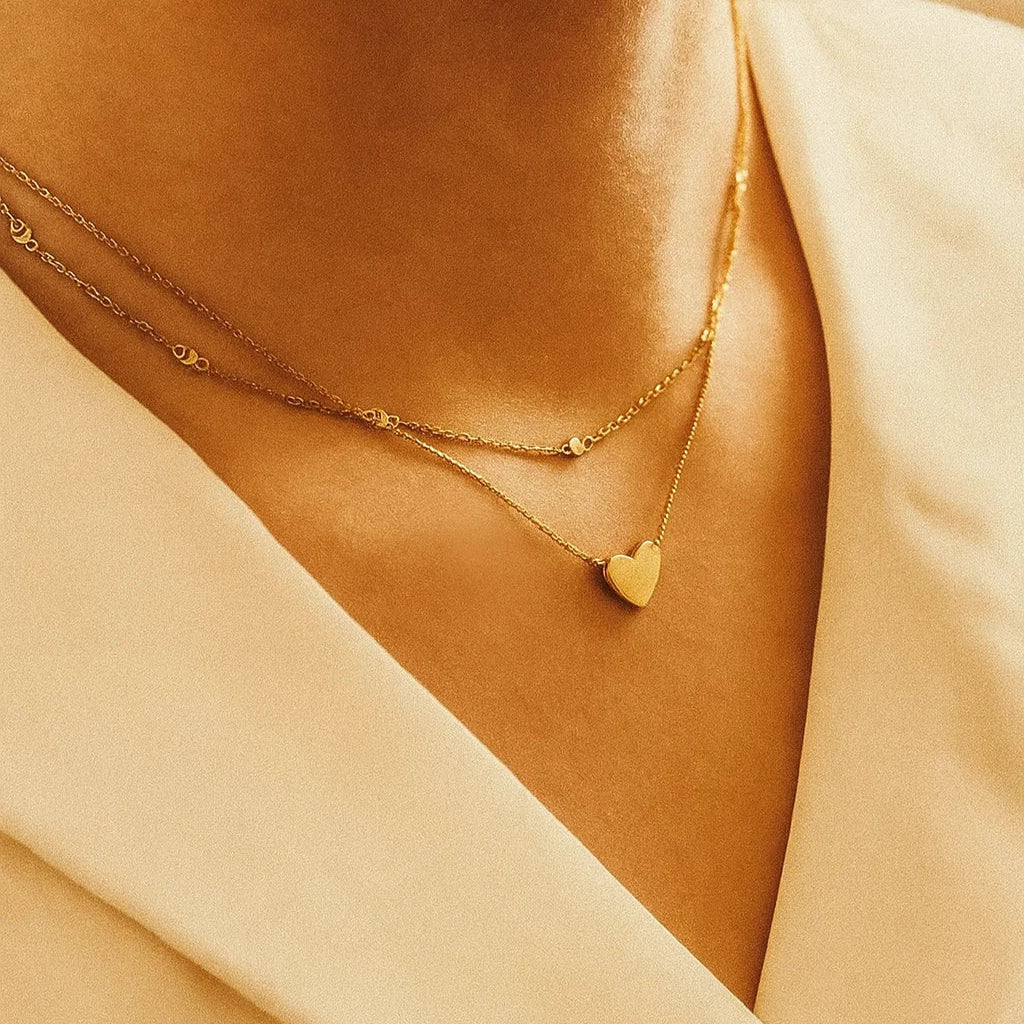 Close-up of a person wearing two AMYO gold necklaces with heart pendants.