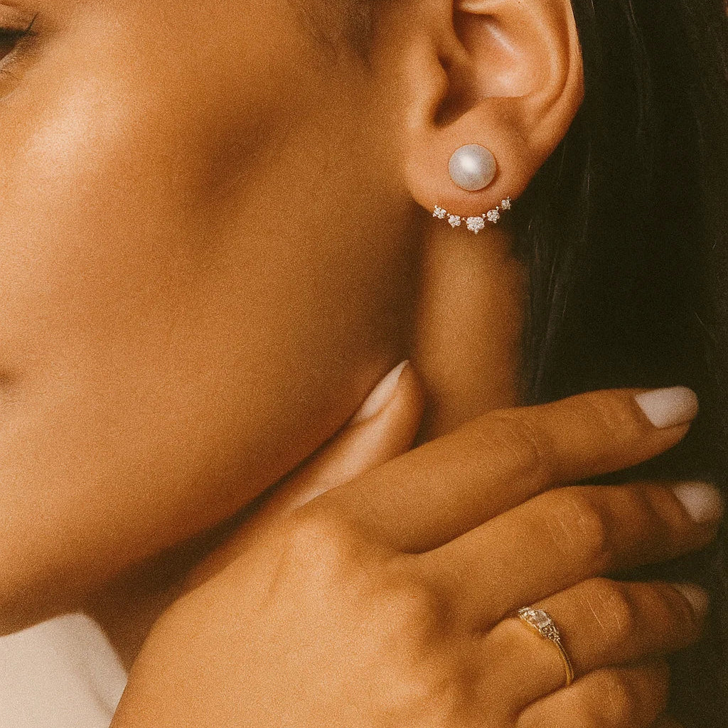 Close-up of a woman's ear wearing AMYO pearl earrings with a hand touching her hair.